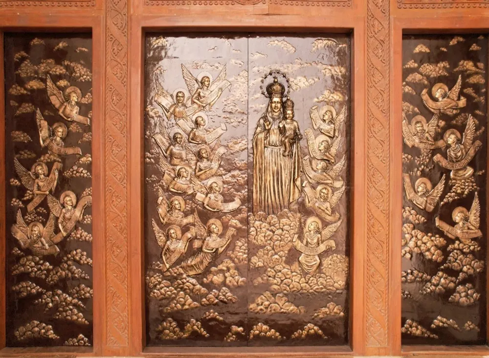 Carved wooden door of the new church, with Our Lady among angels